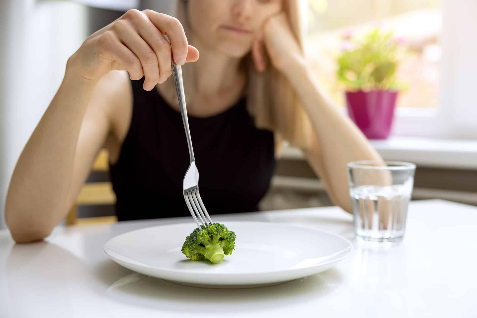 Unhappy woman looking at small broccoli portion on the plate with small glass of water