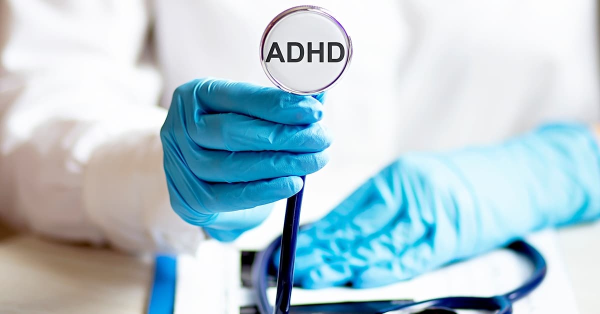 A doctor wearing a white coat and blue latex gloves holds a stethoscope with the text "ADHD" to the camera.