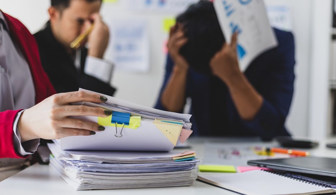 One person grabs a stack of papers. In the background, two businessmen hold their hands up to their heads in distress.
